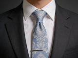 The Ascot Fleur Silk Tie worn in a four-in-hand knot with a white collar and charcoal suit