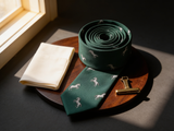 The Ascot Stallion Silk Tie coiled on dark walnut with a pocket square and brass collar bar