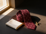 The St. James Medallion Silk Tie coiled on dark walnut with a pocket square and brass collar bar