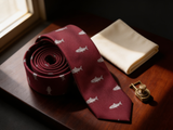 The Speyside Salmon Silk Tie coiled on dark walnut with a pocket square and brass collar bar