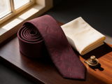 The Sovereign Geometric Silk Tie coiled on dark walnut with a pocket square and brass collar bar
