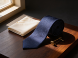 The Regent Midnight Paisley Tie coiled on dark walnut with a pocket square and brass collar bar