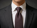 The Westminster Burgundy Basketweave Tie worn in a four-in-hand knot with a white collar and charcoal suit