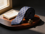 The Regent Silver Geometric Tie coiled on dark walnut with a pocket square and brass collar bar