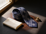 The Mayfair Navy Diamond Tie coiled on dark walnut with a pocket square and brass collar bar