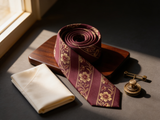 The Highgrove Burgundy Floral Tie coiled on dark walnut with a pocket square and brass collar bar
