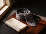 The Shard Geometric Prism Tie coiled on dark walnut with a pocket square and brass collar bar