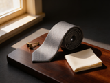 The Regent Geometric Diamond Tie coiled on dark walnut with a pocket square and brass collar bar