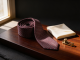 The Knightsbridge Basketweave Tie coiled on dark walnut with a pocket square and brass collar bar