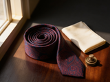 Heritage Paisley Tie coiled on dark walnut with a pocket square and brass collar bar