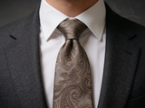 The Belgravia Taupe Paisley Tie worn in a four-in-hand knot with a white collar and charcoal suit