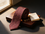 The Sovereign Crown & Crest Tie coiled on dark walnut with a pocket square and brass collar bar