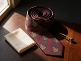 Crested Regimental Charcoal & Crimson Tie coiled on dark walnut with a pocket square and brass collar bar