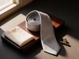 Sovereign Silver Rosette Tie coiled on dark walnut with a pocket square and brass collar bar