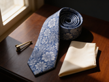 Floral Brocade Navy & Silver Tie coiled on dark walnut with a pocket square and brass collar bar