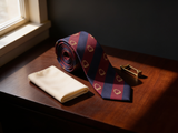 Ascot Stirrup Striped Tie coiled on dark walnut with a pocket square and brass collar bar