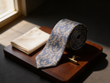 Royal Damask Tie coiled on dark walnut with a pocket square and brass collar bar