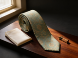 Sage Brocade Floral Tie coiled on dark walnut with a pocket square and brass collar bar