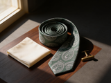 Sovereign Paisley Emerald Tie coiled on dark walnut with a pocket square and brass collar bar