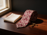 Royal Crown Burgundy Tie coiled on dark walnut with a pocket square and brass collar bar